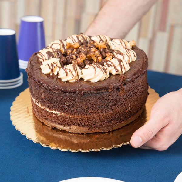A person holding a chocolate cake on a gold cake circle.