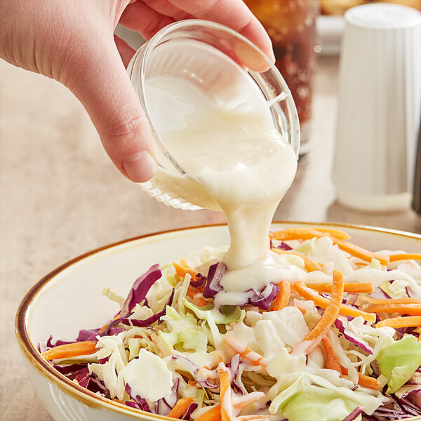 A person pouring Kraft Coleslaw Dressing into a bowl of coleslaw.