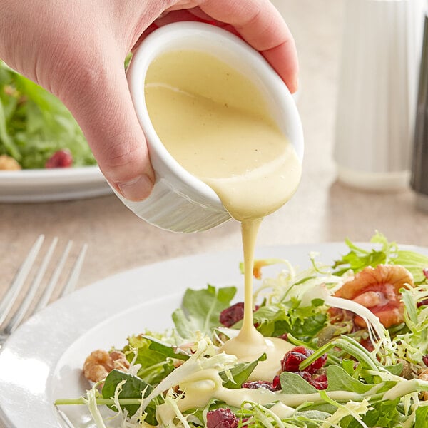 A person pouring Kraft Signature Honey Dijon dressing on a salad.