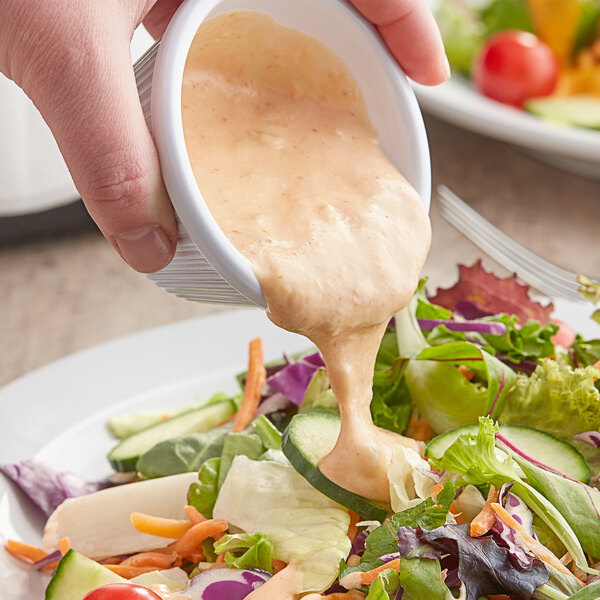 A person pouring Kraft Thousand Island dressing into a bowl of salad.