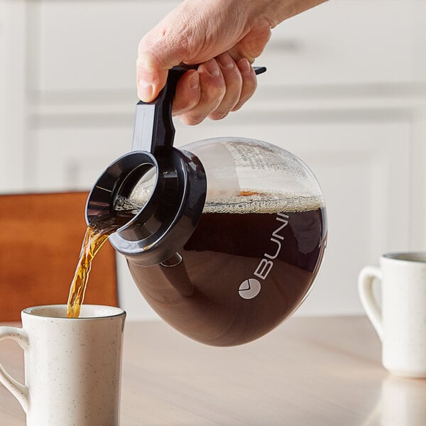 A hand pouring coffee into a Bunn coffee decanter.