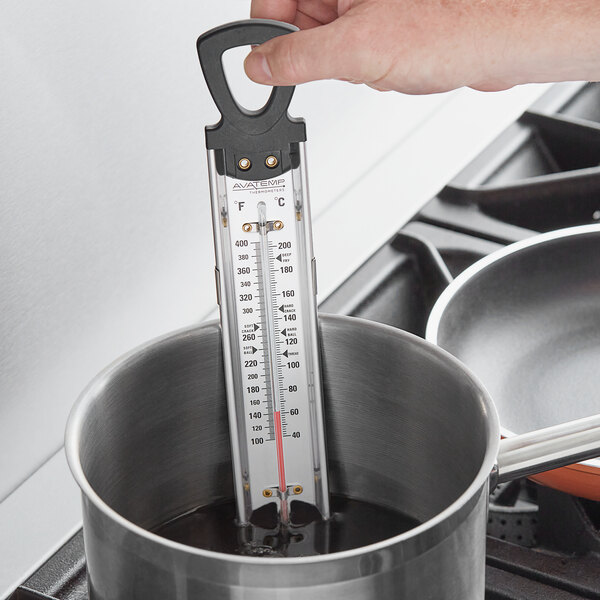 A person using an AvaTemp candy/deep fry thermometer in a pot of liquid.