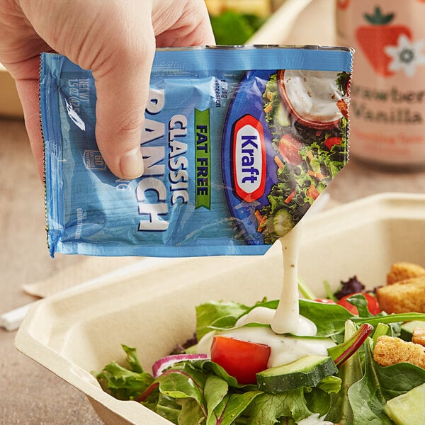 A hand pouring Kraft Fat-Free Ranch dressing from a packet onto a salad.
