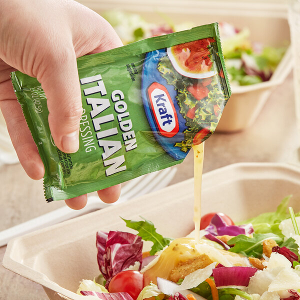 A hand pouring a Kraft Golden Italian dressing packet onto a salad.