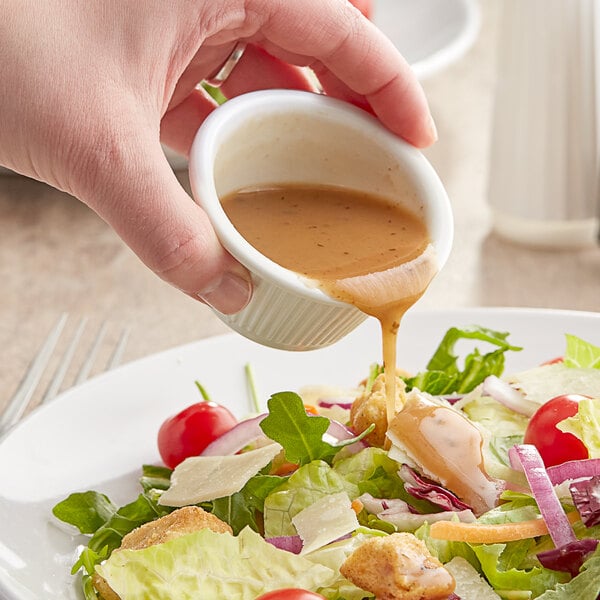 A person pouring Kraft Signature Balsamic Vinaigrette over a bowl of salad.
