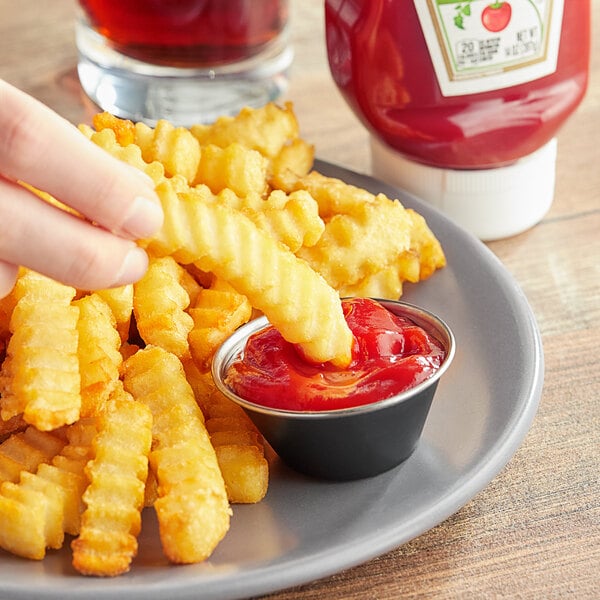 A person dipping french fries into Heinz Organic Ketchup on a plate.