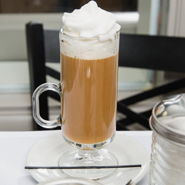 A Libbey Irish glass coffee mug on a plate with a brown drink and white foam.