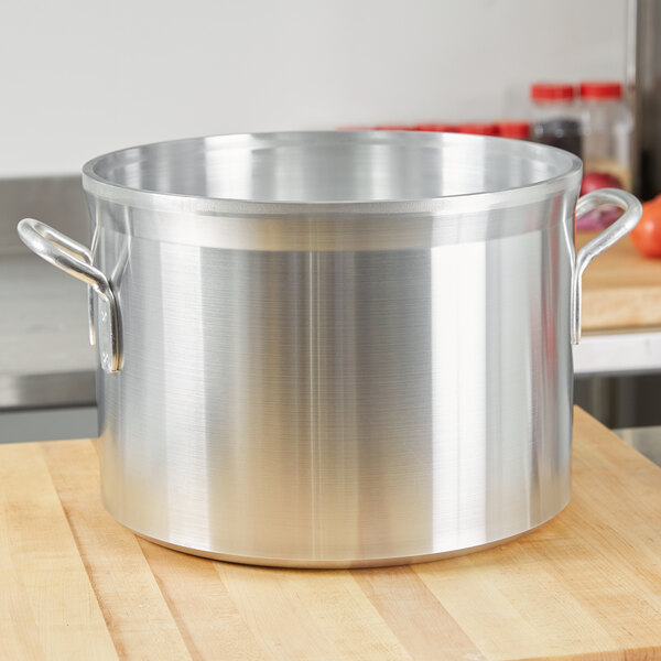 A large silver sauce pot on a wooden surface.