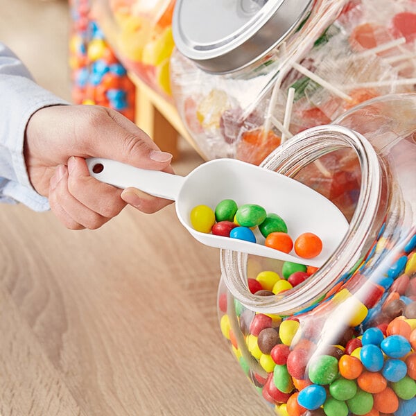 A person holding a white Choice plastic scoop over a jar of candy.