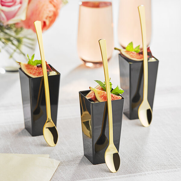 A group of black cups with figs and gold Visions plastic tasting spoons.