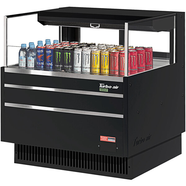 A Turbo Air black horizontal refrigerated open curtain merchandiser on a counter with cans of soda and different colored cans inside.