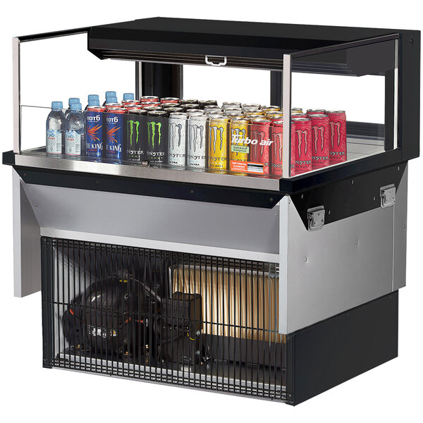 A Turbo Air drop-in refrigerated display case with cans of soda on a counter.