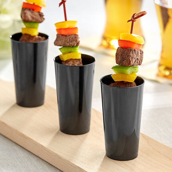 A group of black cups with meat and vegetables on skewers inside.