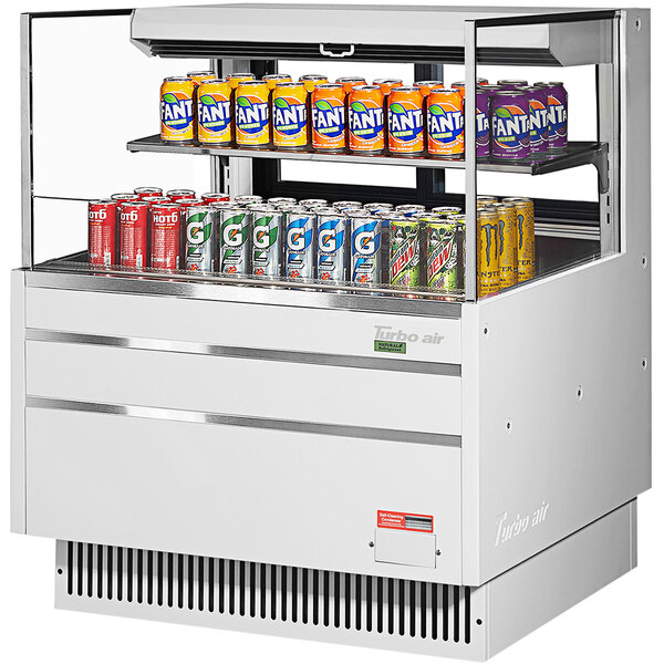 A Turbo Air white refrigerated open curtain merchandiser with cans of soda on the shelf.