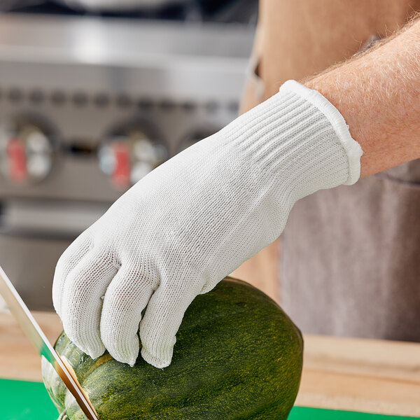 A person wearing a Choice Level A6 cut-resistant glove cutting a cucumber.