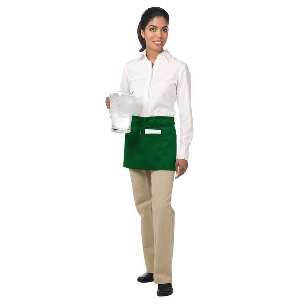 A woman wearing a Chef Revival green waist apron with three pockets.