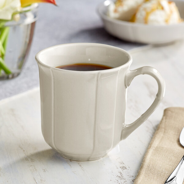 A white Acopa Condesa porcelain mug on a table with coffee in it.