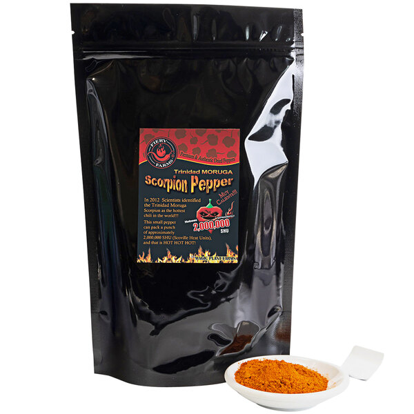 A black bag of Fiery Farms red Trinidad Moruga Scorpion pepper powder with a red label next to a bowl of orange powder.