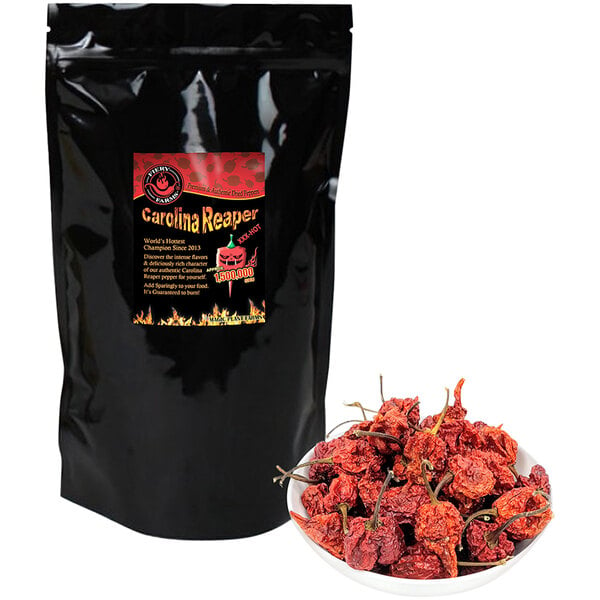 A bowl of Fiery Farms dried red Carolina Reaper pepper pods next to a bag of hot chili peppers.