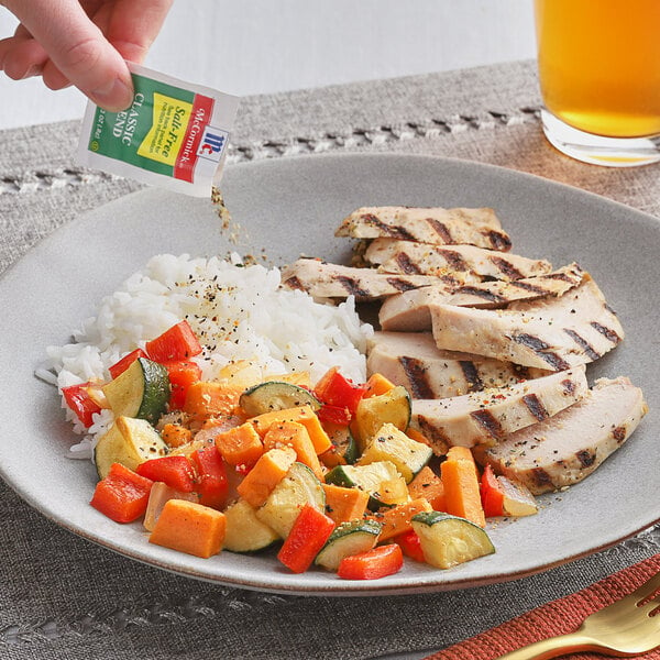 A hand pouring McCormick Salt-Free Classic Seasoning Blend on a plate of food.