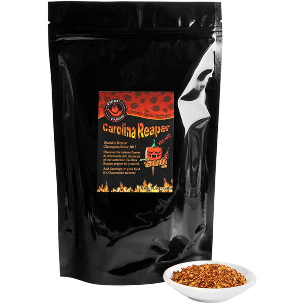 A black bag of Fiery Farms Red Carolina Reaper Pepper Flakes on a counter with a white bowl of flakes.