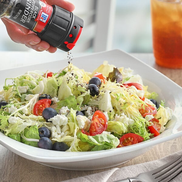 A hand using a McCormick Black Peppercorn Grinder to add pepper to a salad.