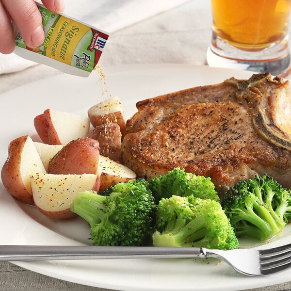 A hand adding McCormick Perfect Pinch seasoning to a plate of meat with potatoes and broccoli.