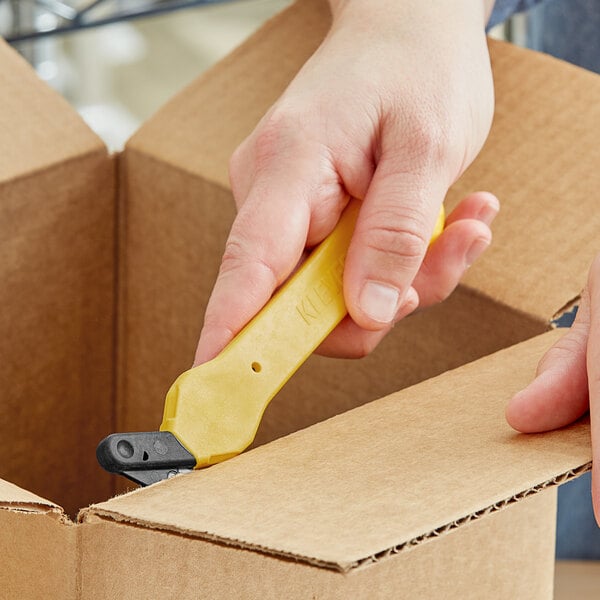 A hand using a yellow Klever Kutter Excel to open a box.