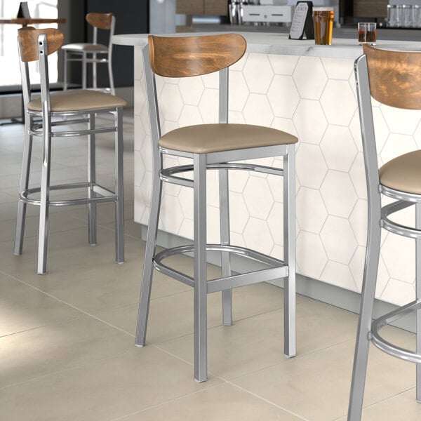 Lancaster Table & Seating Boomerang Series bar stools with taupe vinyl seats and vintage wood backs at a restaurant counter.