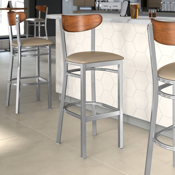 Lancaster Table & Seating Boomerang bar stools with taupe vinyl seats and wood backs at a restaurant counter.