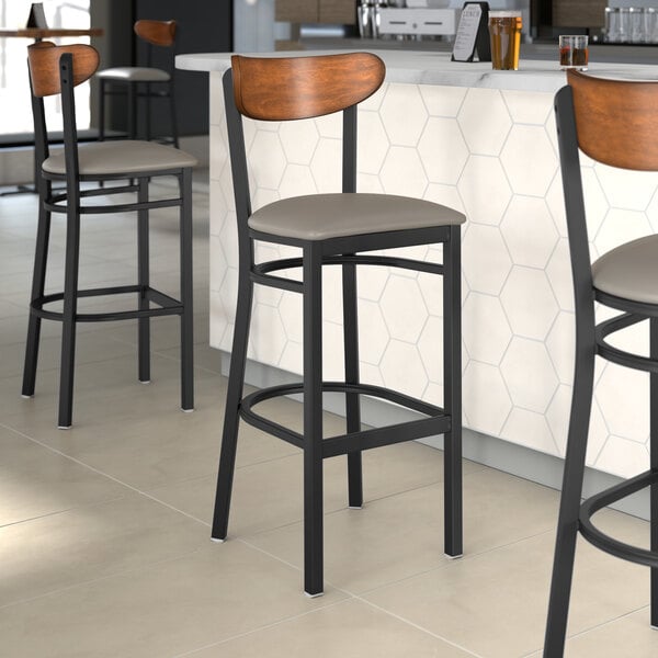 Lancaster Table & Seating bar stools with dark gray vinyl seats and antique walnut backs at a restaurant counter.