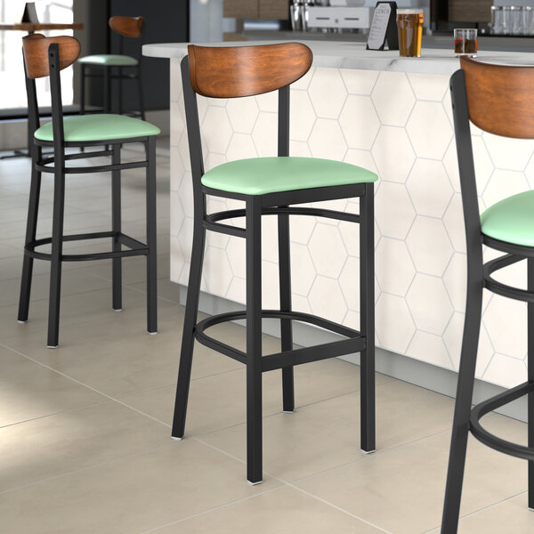 A group of Lancaster Table & Seating bar stools with seafoam vinyl seats and antique walnut backs.
