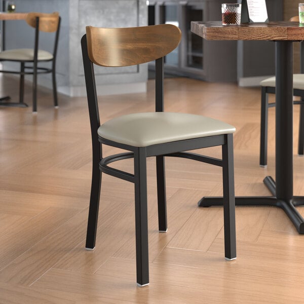 A Lancaster Table & Seating Boomerang Series chair with a light gray vinyl seat and vintage wood back in a restaurant.