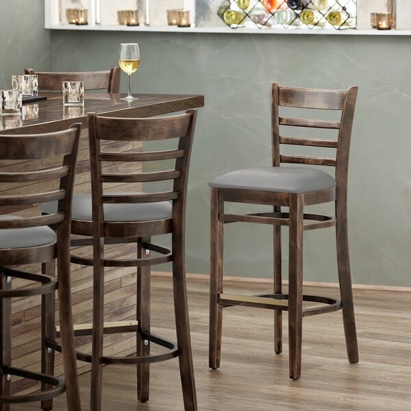 A Lancaster Table & Seating wood ladder back bar stool with a light gray vinyl seat on a table in a restaurant.