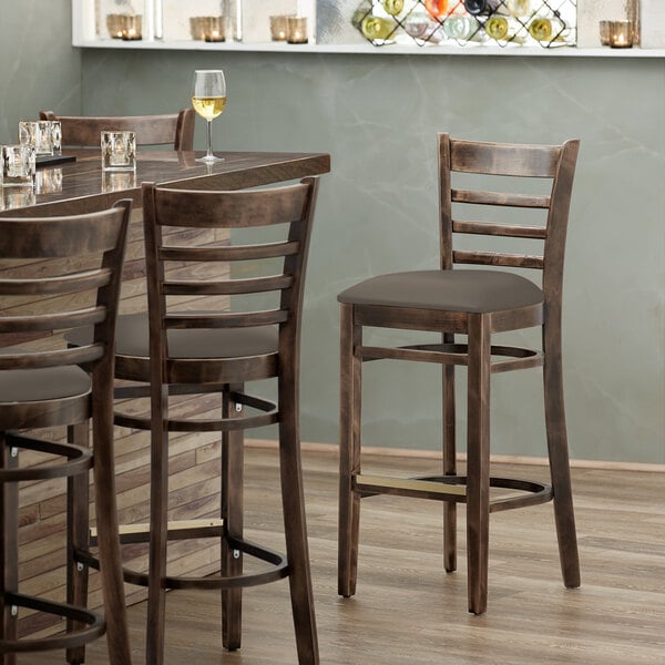 A Lancaster Table & Seating wood ladder back bar stool with a taupe vinyl seat on a table in a restaurant.