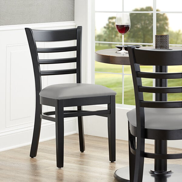 A black Lancaster Table & Seating wood ladder back chair with a light gray vinyl seat at a table in a restaurant.