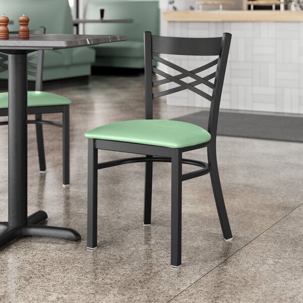 A Lancaster Table & Seating black cross back chair with a seafoam green vinyl cushion on a restaurant table.