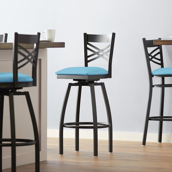 A Lancaster Table & Seating black metal swivel bar stool with a blue cushion.