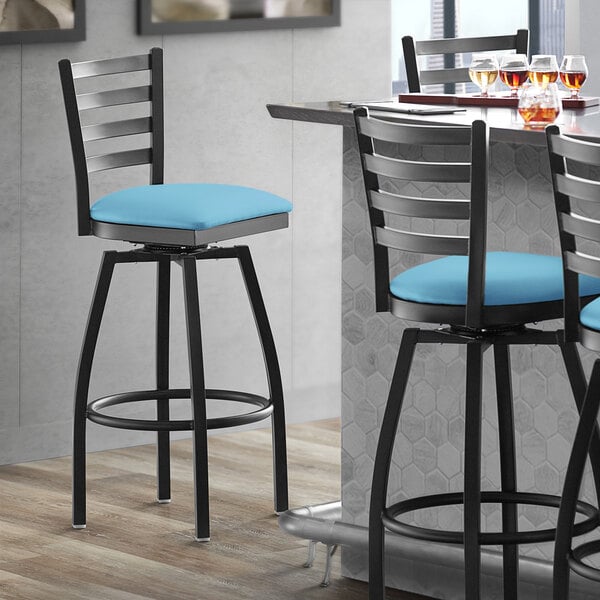 A Lancaster Table & Seating black ladder back swivel bar stool with a blue cushion.