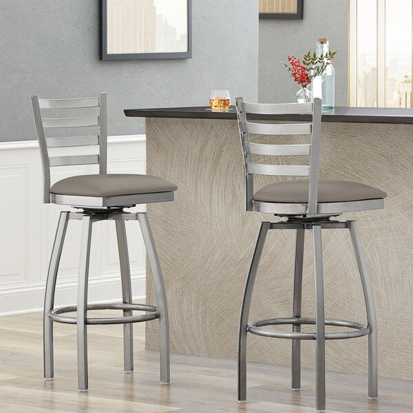 Two Lancaster Table & Seating ladder back bar stools with dark gray vinyl padded seats at a counter.