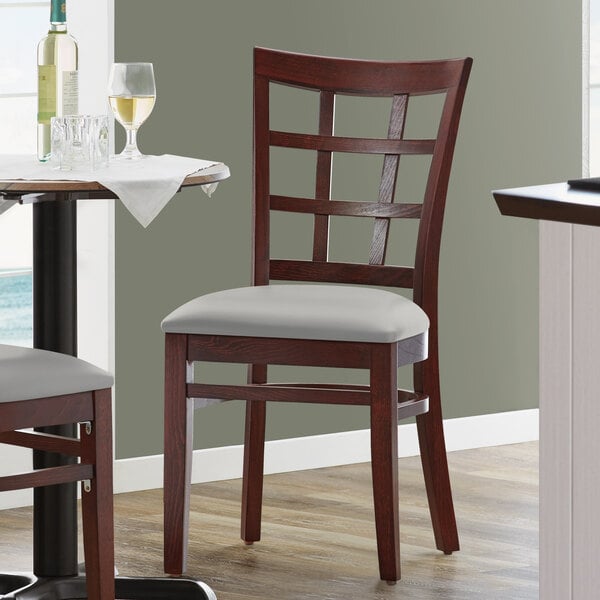 A Lancaster Table & Seating wood chair with a light gray cushion on a table in a restaurant.