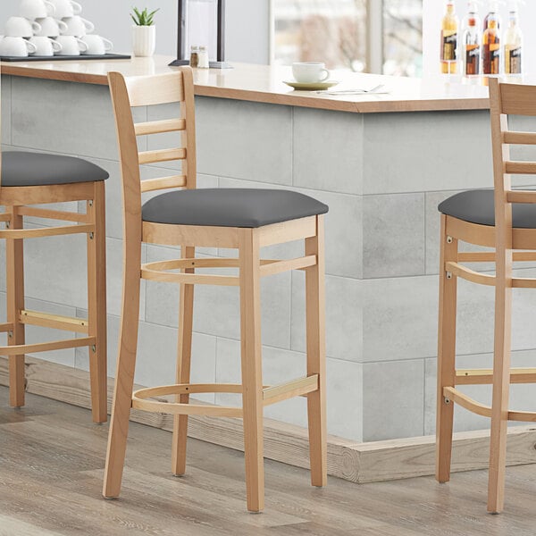 Three Lancaster Table & Seating wooden ladder back bar stools with dark gray vinyl seats at a kitchen counter.