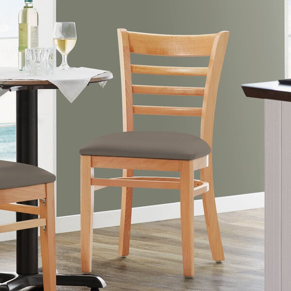 A Lancaster Table & Seating wooden ladder back chair with a taupe vinyl seat.