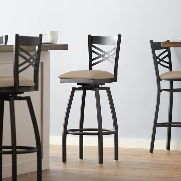 A Lancaster Table & Seating black swivel bar stool with taupe vinyl padded seat.