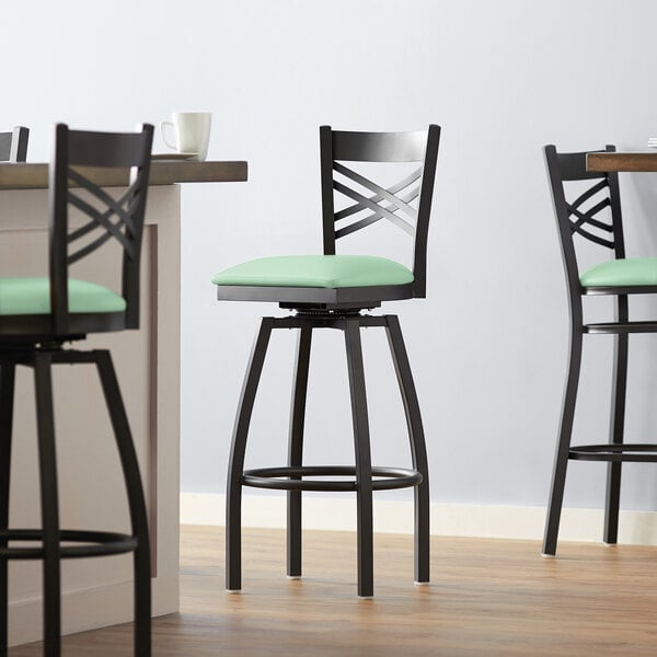A Lancaster Table & Seating black cross back swivel bar stool with a seafoam green cushion.