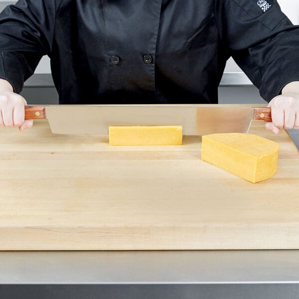 A person uses a Dexter-Russell double wooden handled cheese knife to cut cheese on a cutting board.