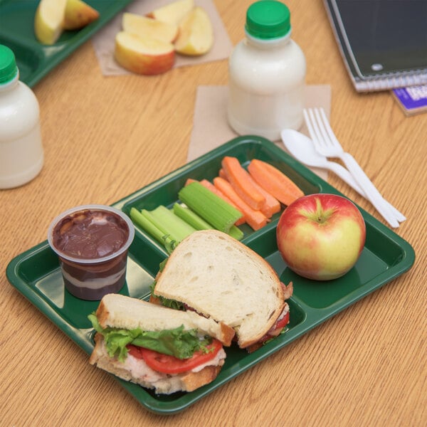 A forest green Carlisle 4 compartment tray with a sandwich, apple, and juice.
