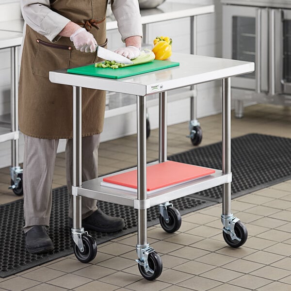 A chef cutting vegetables on a Regency stainless steel work table with casters.