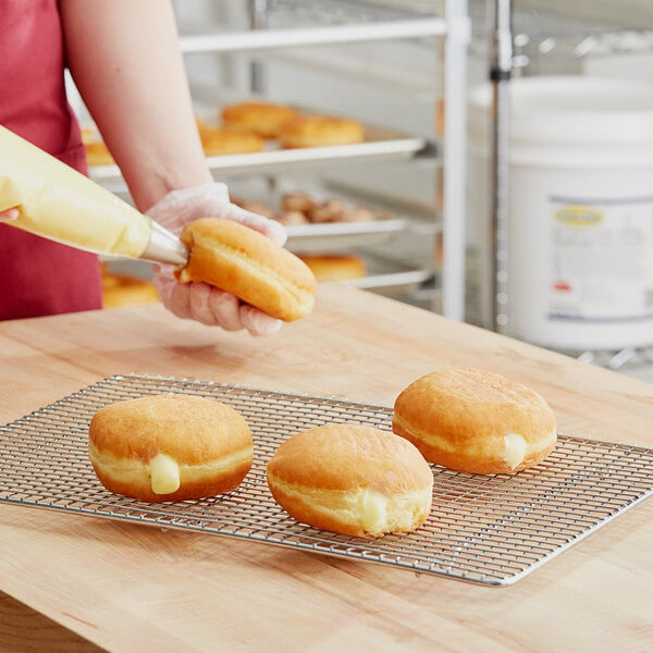 A person putting Rich's Bavarian creme on a doughnut on a wire rack.