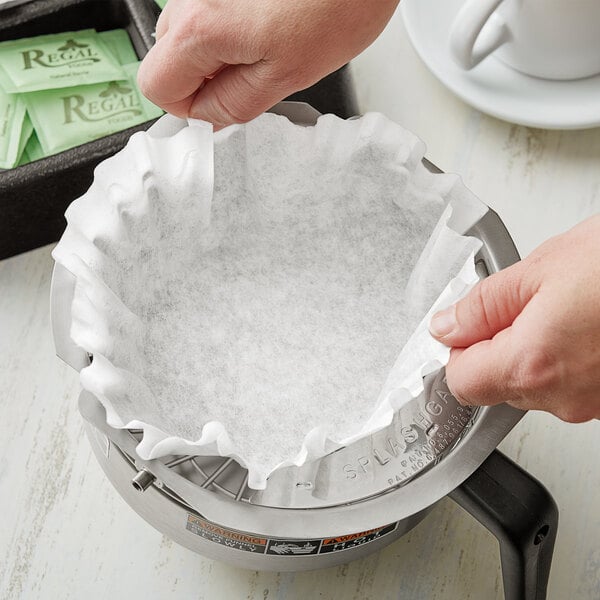 A person's hands using a Choice paper coffee filter over a coffee maker.